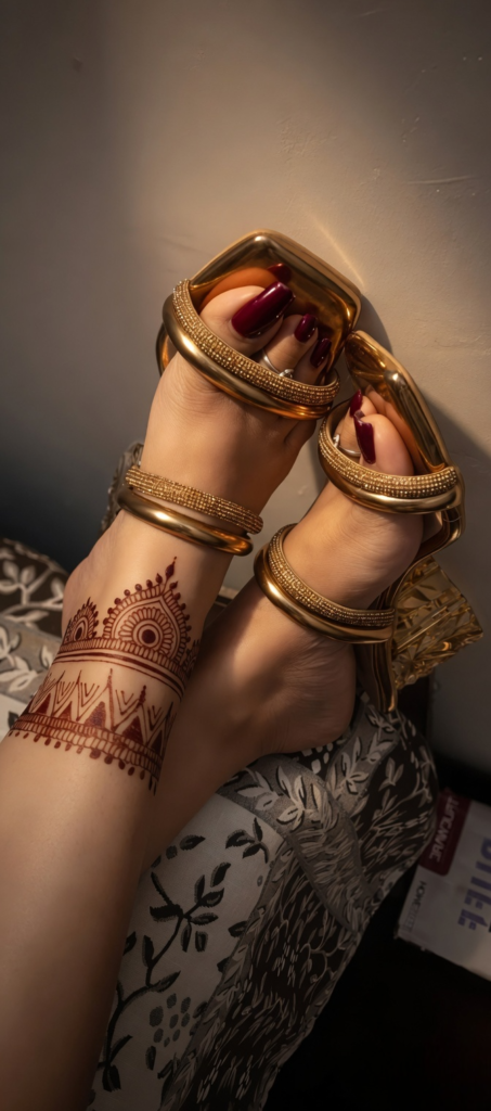 Elegant feet of Sharjah BDSM Mistress Anu adorned with beautiful henna tattoo art, wearing glamorous gold strap heels.